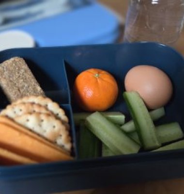 Photograph of a lunchbox containing cheese, crackers, flapjack, satsuma, egg and cucumber