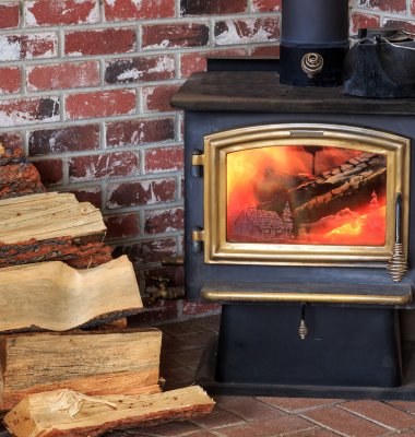 Photograph of a lit wood burner with a pile of logs at the side