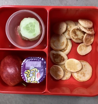 Photograph of pupil's packed lunch containing mini pancakes, cucumber, apple and yoghurt