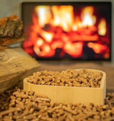 Photograph of a heart-shaped container full of eco-fuel with a lit wood burner in the background