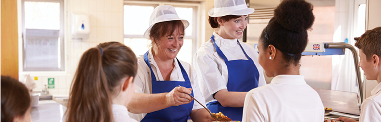 A photograph of two school dinner ladies serving three children food