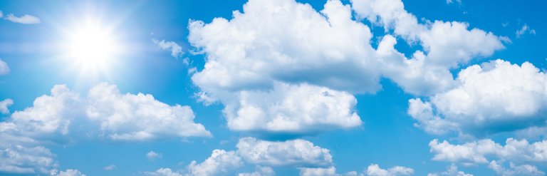 Photograph of sun shining in a blue sky with patches of cloud